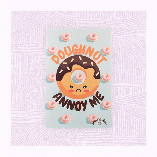 Postcard art print with a blue background and pink doughnuts, and an angry looking doughnut character with the phrase ‘Doughnut Annoy Me’.