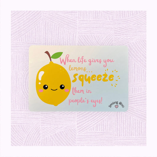 Postcard art print with a blue into yellow faded background, a cute lemon character in the foreground with the phrase ‘When life gives you lemons, squeeze them in people’s eyes’.