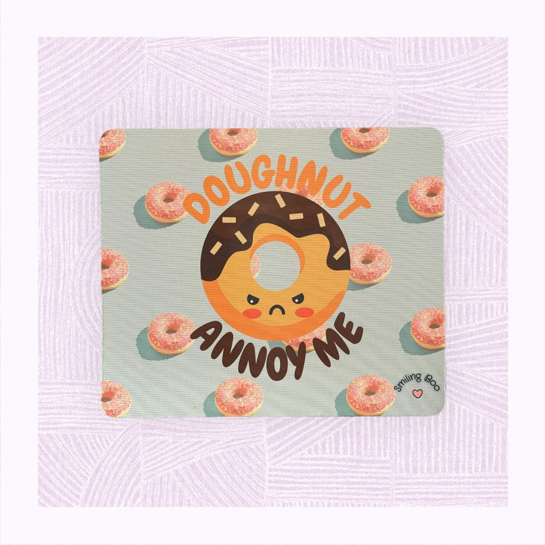 Rectangle mouse mat with a blue background and pink doughnuts, and an angry looking doughnut character with the phrase ‘Doughnut Annoy Me’.