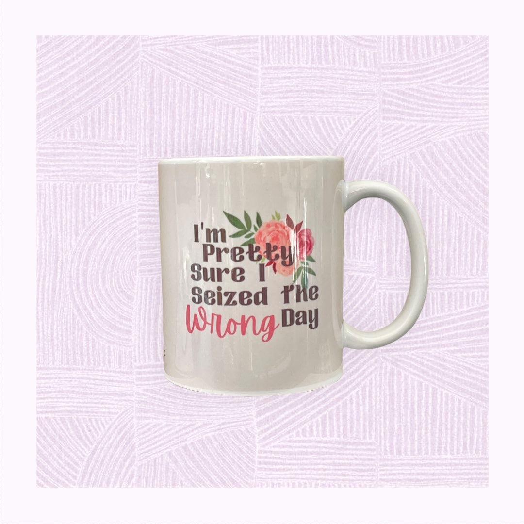 Ceramic mug with a pastel pink/peach watercolour background with the phrase ‘I’m pretty sure I seized the wrong day’ and floral arrangement